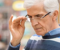 A picture of an older man wearing glasses and holding it with his hand.