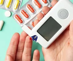 An image showing hands with a diabetes monitoring device and some pills placed on a table.