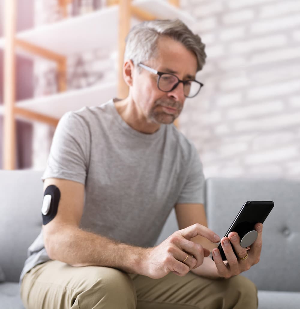 In this image, a man holds a mobile phone and monitor blood glucose.